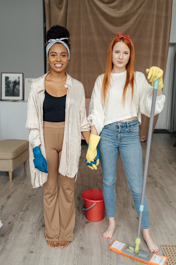 Two women smiling and holding hands while cleaning indoors, symbolizing teamwork.